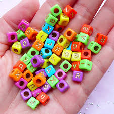 A hand holds colorful alphabet beads in various bright hues like orange, green, pink, and blue. Each bead has a different letter, creating a playful and cheerful vibe.